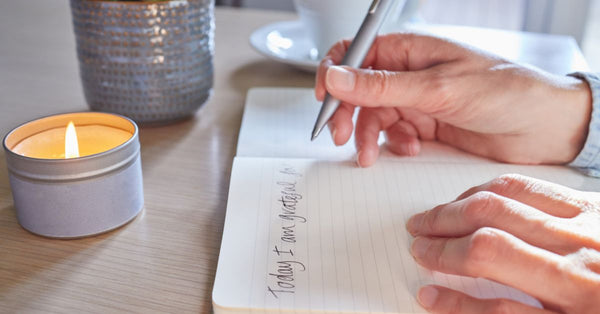 Person writing gratitude journal by lit candle illustrating the benefits of gratitude for mental health