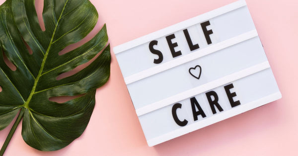 Lightbox sign displaying self care text beside large green leaf showing how to create a holiday self-care plan