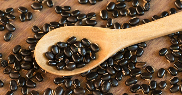 Close-up of Mucuna pruriens velvet bean seeds on a wooden spoon and surface showing how does mucuna pruriens help with stress