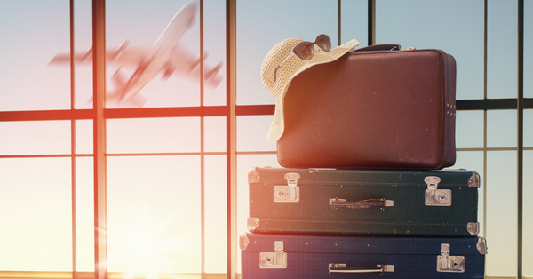 Stacked suitcases with a sun hat and sunglasses near airport window during sunset showcasing holiday travel sleep tips
