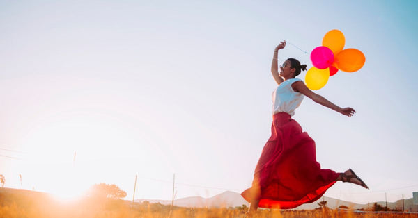 Woman joyfully jumping outdoors holding colorful balloons showing how to reduce stress and increase joy in 2025